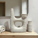 White ceramic candle holders with architectural U-shape design displayed on wooden shelf with mirror