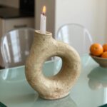 Speckled ceramic candle holder closeup on glass table, handmade ring-shaped pottery with organic texture and lit candle