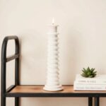 Rustic white ceramic candle holder with textured grooves and lit candle in bedroom setting