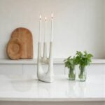 Artisan ceramic candle holder with hand silhouette design holding three white taper candles on shelf