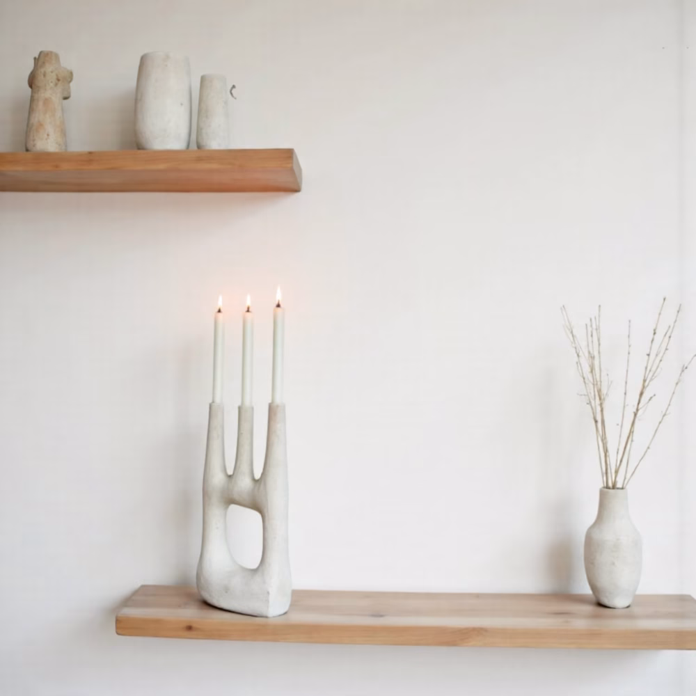 White triple candle holder on wooden shelf with dried flowers