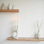 Sculptural white ceramic candle holder with abstract hand form on wood shelf with dried florals