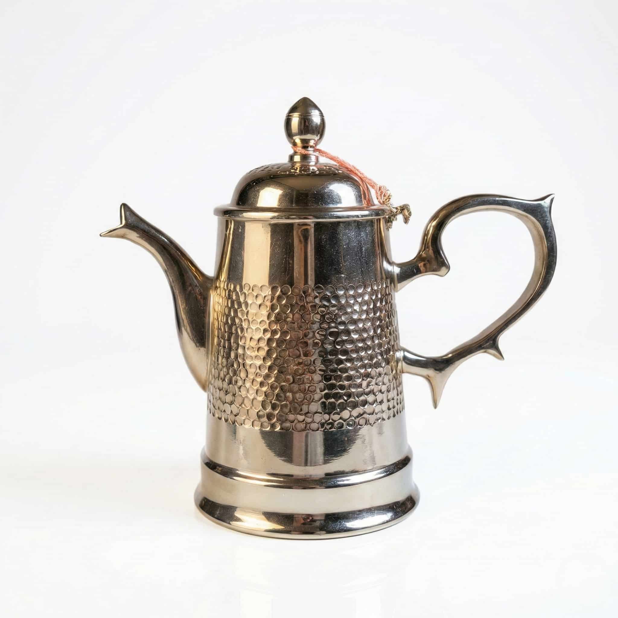 silver-plated brass coffee pot (1) Moroccan silver-plated brass coffee pot with hammered dot pattern and orange silk tassel shown on white background