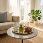 A collection of white geometric tea glasses served with fresh mint tea, arranged on a traditional round brass tray alongside sweet Moroccan pastries on a marble coffee table in an airy living room.