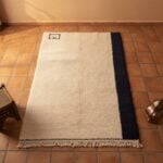 Modern wool rug on terracotta tile floor featuring handwoven cream texture and bold navy border accent