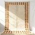 Handwoven wool rug with cream pile and terracotta border squares displayed vertically on white wall