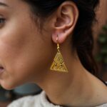 Woman wearing gold geometric brass earrings with tribal mountain motif and antiqued finish