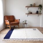 Modern wool rug with navy border near leather chair showing plush cream pile and Greek key corner design