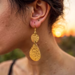 Gold drop earrings shown on model at sunset