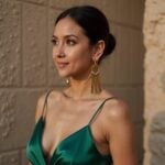 Woman wearing gold brass fringe earrings with geometric stick drop design and green satin dress
