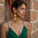 Woman wearing gold hammered brass earrings in green dress, side profile showing teardrop dangle earrings