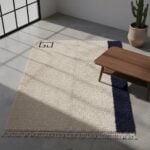 Modern wool rug detail showing high-pile cream texture with navy border and decorative fringe trim