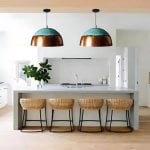 Two verdigris copper brass pendant lights hung over modern kitchen island with natural wood bar stools