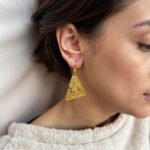 Close-up of handmade geometric brass earrings featuring tribal patterns and gold antiqued finish