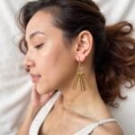 Close-up of brass fringe earrings showing handcrafted gold metal spike details radiating from circular ring