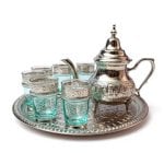 Silver tea set with ornate engraved teapot, turquoise glass holders & decorative tray on white background