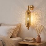 Brass wall sconce installed in bedroom casting warm geometric shadow patterns on wall, styled with neutral linen bedding and pampas grass