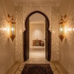 Pair of brass wall sconces flanking traditional arched doorway in riad-style hallway, projecting intricate light patterns across marble floors