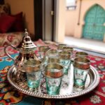 Silver engraved beldi tea set with aqua glasses and footed teapot on an ornate round tray over a patterned rug