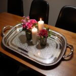 Oval serving tray in silver-plated brass holding candles and pink roses on a dark wooden dining table