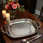 Silver-plated brass oval serving tray with floral arrangement and lit candles on wooden dining table