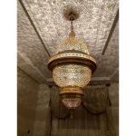 Illuminated engraved brass pendant light creating intricate lace-like shadow patterns on ceiling and walls