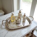 Silver-plated brass oval serving tray on white marble countertop holding cosmetics and perfume bottles