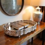 Hammered silver tray with ornate filigree border on dark wooden console table