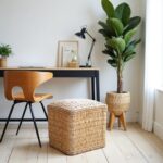 Natural straw ottoman pouf placed next to modern desk with fiddle leaf plant