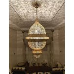 Engraved brass pendant light illuminated, casting ornate shadow patterns on ceiling in bedroom interior