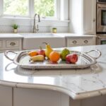 Oval serving tray in silver-plated brass holding fresh pears and oranges on white marble countertop