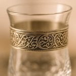 Silver engraved glass tea set with red tassel teapot and 6 glasses on decorative tray, garden backdrop