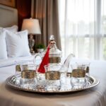 Silver engraved glass tea set arranged on white bed linens in a bedroom interior