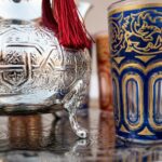 Extreme close-up of the hand-chiseled geometric details on a teapot and the gold-leaf patterns on a blue glass from a moroccan mint tea set.