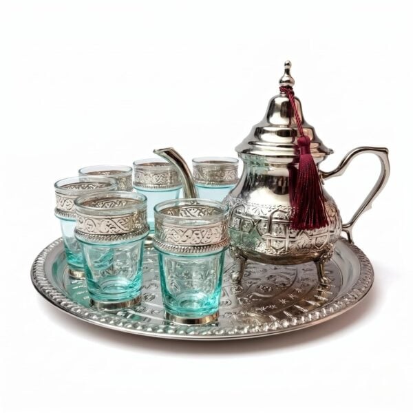 Silver engraved beldi tea set featuring an authentic Moroccan teapot adorned with a burgundy tassel, six blue-tinted glasses with intricate engraved silver metal sleeves, and a coordinating round serving tray, isolated on a bright white background.