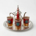 A small moroccan tea set with a silver teapot and three glasses featuring a teal Moroccan star design, displayed on a clean white background.