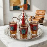 Close-up of engraved silver teapot with red silk tassel from a small moroccan tea set on a white background