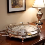 Hand-engraved silver large round tray displayed on wooden sideboard with silver lamp and artwork