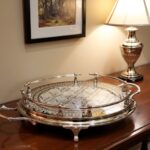 Large silver tray on wooden sideboard beside silver lamp and framed artwork