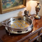 Silver and gold big round tray displayed on wooden console table with decorative lamp and artwork