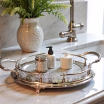 Silver hand-engraved large round tray with handles displaying luxury skincare products on marble bathroom counter