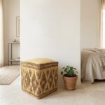 Woven square straw floor pouf styled next to a small potted plant in a modern minimalist interior space.