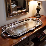 Decorative silver serving tray on wooden console table with matching mirror and lamp
