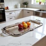 Rectangular silver tray with hand-engraved floral border holding fresh fruit on white marble countertop