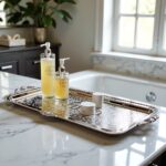 Silver serving tray organizing skincare bottles on white marble bathroom vanity