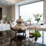 Silver teapot wheat leaf design on black marble table with gold-rimmed Moroccan tea glasses and fresh mint
