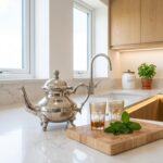 Polished silver teapot wheat leaf design on white quartz countertop with fresh mint and wooden cutting board