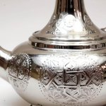 Close-up of hand-engraved silver teapot showing intricate geometric patterns and floral medallion details