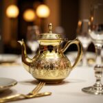 Polished gold brass teapot hand-engraved with geometric patterns on a wooden dining table setting