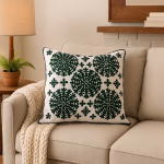 Forest green embroidered medallion cushion cover on beige sofa with chunky knit throw, styled with wooden lamp and potted fern in neutral living room setting